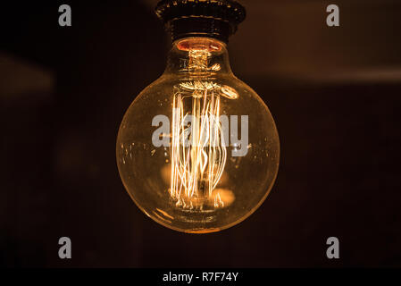 Large long electric incandescent filament in a retro style light bulb glows and reflects warm light. Stock Photo