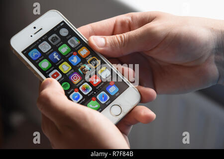 Teenage boy holding a Apple iPhone SE mobile phone displaying various appts. Stock Photo