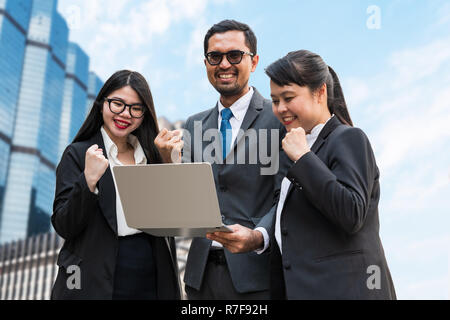 Two business women and a business man clenching their fists looking at the laptop screen with the happy smiling faces Stock Photo
