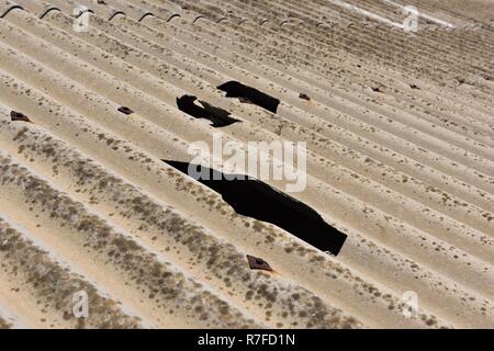 Holes in the corrugated asbestos cement roof covering Stock Photo