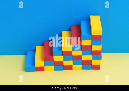 multi colored stairway, formed by wooden toy blocks, in front of a blue wall Stock Photo