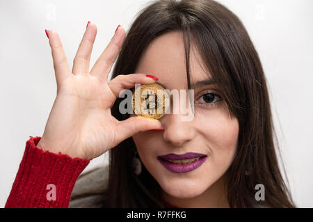 Woman Holding a Bitcoin in front of her right eye Stock Photo