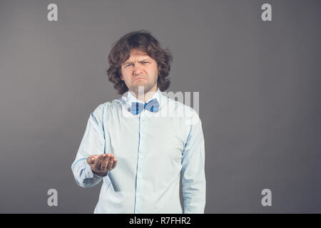 Man in business shirt and blue bow tie shows outstretched hand with open palm. Unhappy sad man asks for money. Lack of money concept. Asking for help, financial assistance. Financial meltdown Stock Photo