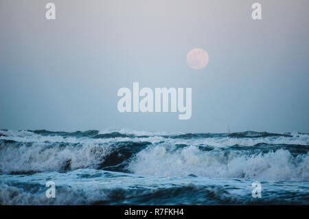 Splashing wave on the Black sea in the night with rising full moon in the background Stock Photo