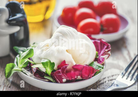 Burato cheese and lettuce for weight correction of Lollo Rosso lettuce leaves, watercress salad and other green herbs. The concept of healthy eating.  Stock Photo