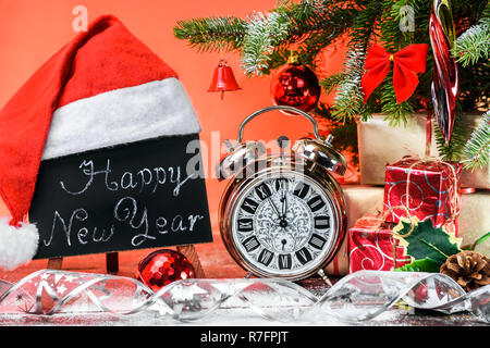 A blackboard with the text 'Happy New Year' written in a chalk covered with a Santa Claus hat on a wooden board covered with snow next to the vintage  Stock Photo