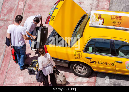 Miami Beach Florida,Ocean Drive,taxi,taxis,cab,cabs,yellow color,man men male,woman female women,couple,driver,trunk,luggage,suitcase,bag,loading,lift Stock Photo