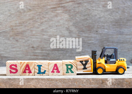 Toy forklift hold letter block Y to complete word salary on wood background Stock Photo