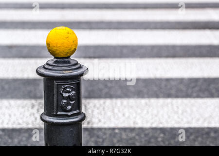 yellow metal ball on parking pole, below Warsaw coat of arms, blurred pedestrian crossing in background Stock Photo