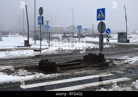 Heavy fog, road works in the city in cloudy snowy weather, repair of a pedestrian crossing, repair of asphalt, installation of road signs. Stock Photo