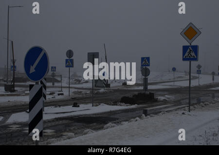 Heavy fog, road works in the city in cloudy snowy weather, repair of a pedestrian crossing, repair of asphalt, installation of road signs. Stock Photo