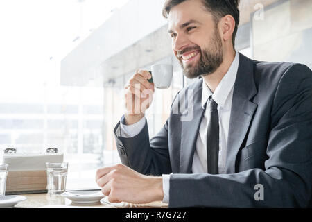 Businessperson on coffee break at restaurant sitting drinking espresso smiling Stock Photo
