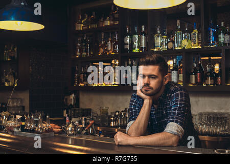 Young bartender leaning on bar counter thoughtful Stock Photo