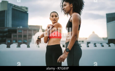 Two female athletes doing workout standing on rooftop. Women in fitness clothes doing fitness training on terrace with high rise buildings in the back Stock Photo