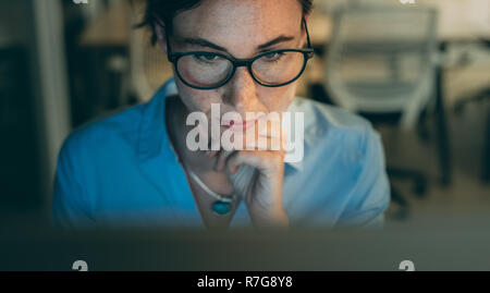 Close up of a businesswoman working on computer in office. Cropped shot of a woman in eyeglasses looking at a computer screen. Stock Photo
