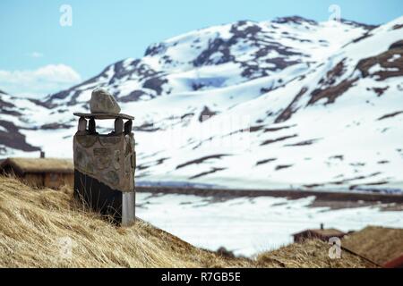 chimneys on the norwegian traditional house and snow capped mountains in the background Stock Photo