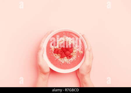 Woman's hands holding raspberries smoothie bowl on pink background. Image toned in trendy Living Coral color. Minimal styled concept. Color of the year 2019. Stock Photo