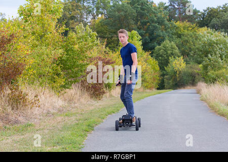 Young european man rides electrical mountainboard on road in nature Stock Photo