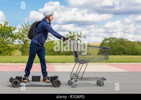 Dutch teenage boy  rides on electric skateboard pushing shopping cart outdoors Stock Photo