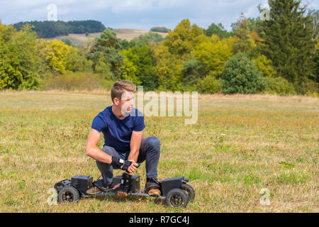 Caucasian teenage boy rides electrical mountainboard in grass field Stock Photo