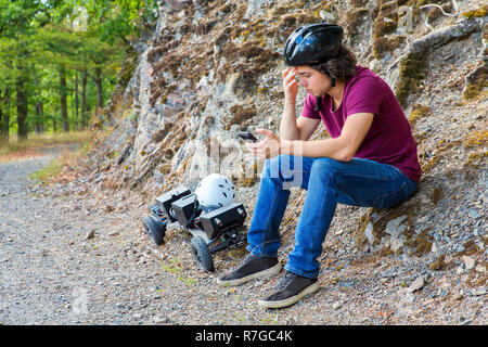 Young caucasian  man sitting on rock with mountainboard and cellphone in nature Stock Photo