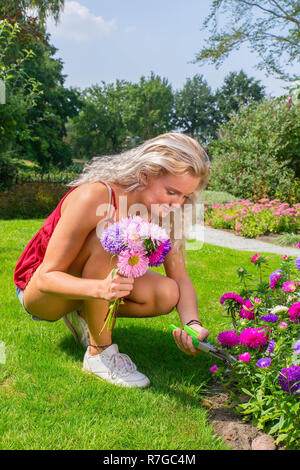 Young caucasian woman pruning colorful summer flowers in garden Stock Photo
