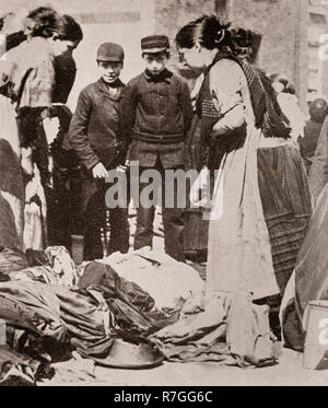 Life for working folk in Victorian days... Examining the goods at the Clothes Market near Fox Street off Scotland Road, later to become known as Paddy's Market, Liverpool, Merseyside, England Stock Photo