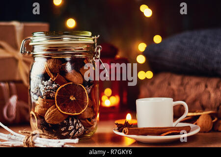 cup of coffee, pine cones, dried oranges and garland lights on dark background. Hygge or cozy home decorations Stock Photo