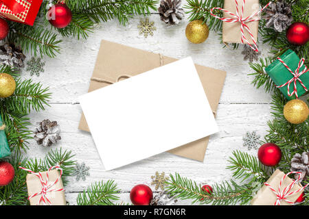 christmas blank greeting card in frame made of fir tree branches, decorations and gift boxes over white wooden table. mock up. flat lay Stock Photo