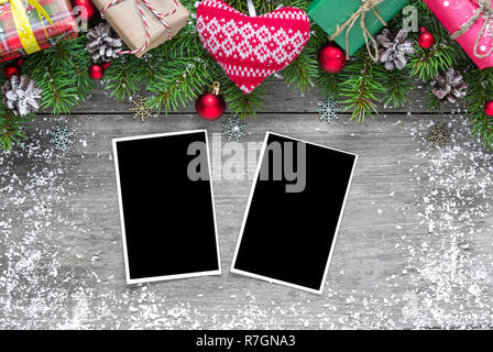christmas blank photo frames with fir tree branches, decorations, gift boxes and knitted heart over rustic wooden background. mock up. flat lay. top v Stock Photo