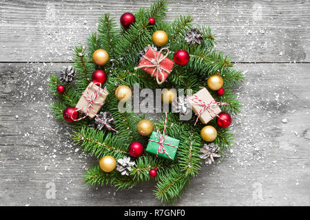 Christmas wreath with decorations and gift boxes on rustic wooden table covered with snow. top view Stock Photo