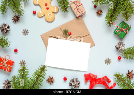 christmas composition with blank greeting card in frame made of fir tree branches, decorations and gift boxes over blue background. mock up. flat lay. Stock Photo