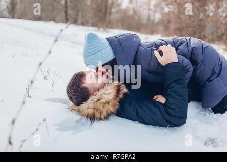Beautiful loving couple lying on snow and kissing in winter forest. People having fun outdoors. Romantic relationships Stock Photo