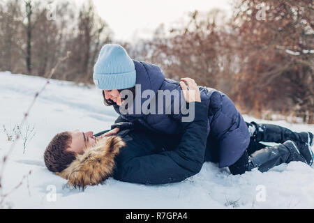 Beautiful loving couple lying on snow in winter forest. People having fun outdoors. Romantic date Stock Photo