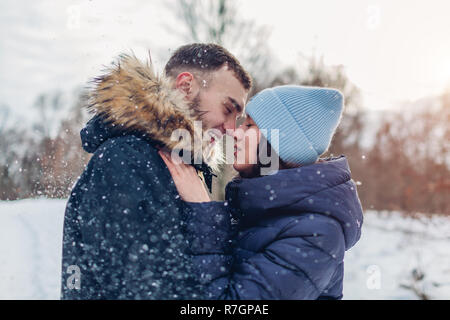 Beautiful loving couple walking and hugging in winter forest. People having fun outdoors under falling snow Stock Photo