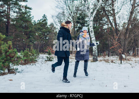 Beautiful loving couple running holding hands in winter forest together. People having fun outdoors Stock Photo