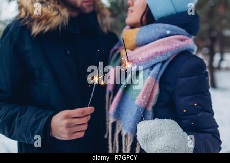 Beautiful loving couple burning sparklers in winter forest. Christmas and New year concept. Close up Stock Photo