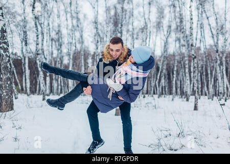 Guy carrying his girlfriend on hands in winter forest. Happy people having fun outdoors Stock Photo