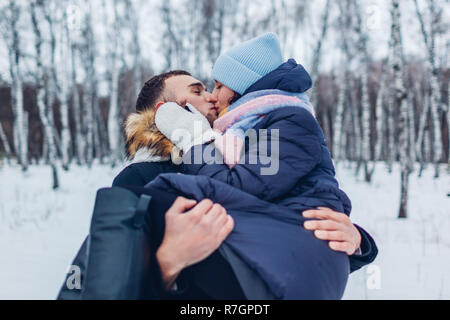 Guy carrying his girlfriend on hands and kissing in winter forest. Happy people having fun outdoors Stock Photo