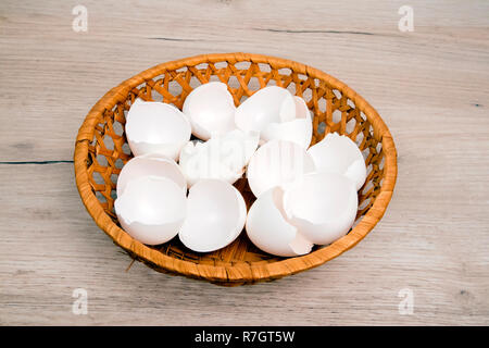 A pile of empty  white egg shells in wicker basket placed on wooden board Stock Photo