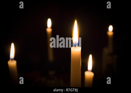 A number of burning melted candles with blurred forks of flame against dark background Stock Photo