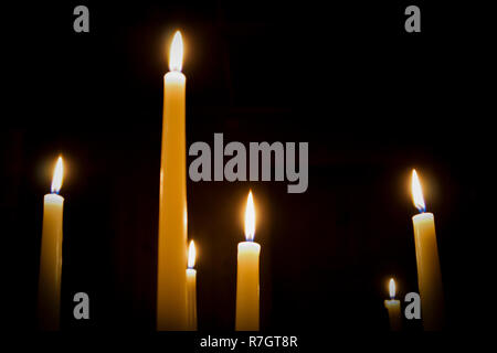 A number of burning melted candles with blurred forks of flame against dark background Stock Photo