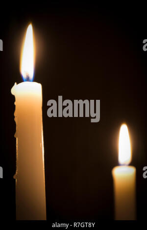 Two burning melted candles with blurred forks of flame against dark background Stock Photo