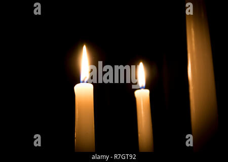 Three burning melted candles with blurred forks of flame against dark background Stock Photo
