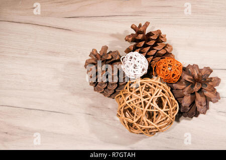 Three dried ripe opened cedar cones and three wicker balls lying on light wooden board Stock Photo