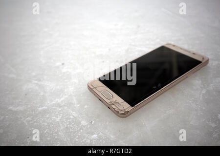 Modern smart phone with cracked screen glass lying on scratched ice Stock Photo