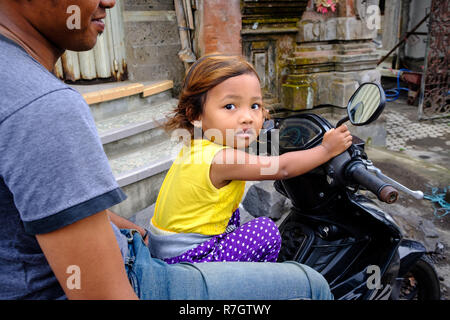 Man and daughter sit on a motorbike at a market in Bali, Indonesia Stock Photo