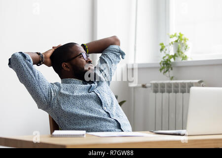 Black relaxed worker sitting on chair looking at window  Stock Photo