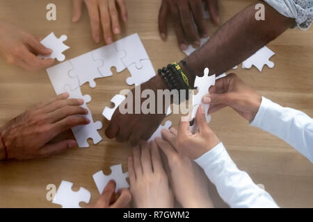 Close up hands from above of diverse people assembling puzzle Stock Photo