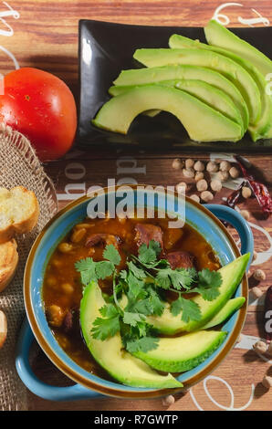 stew of chorizo and chickpeas, on a blue plate with avocado and toast garnished with cilantro on a table decorated in low key light Stock Photo